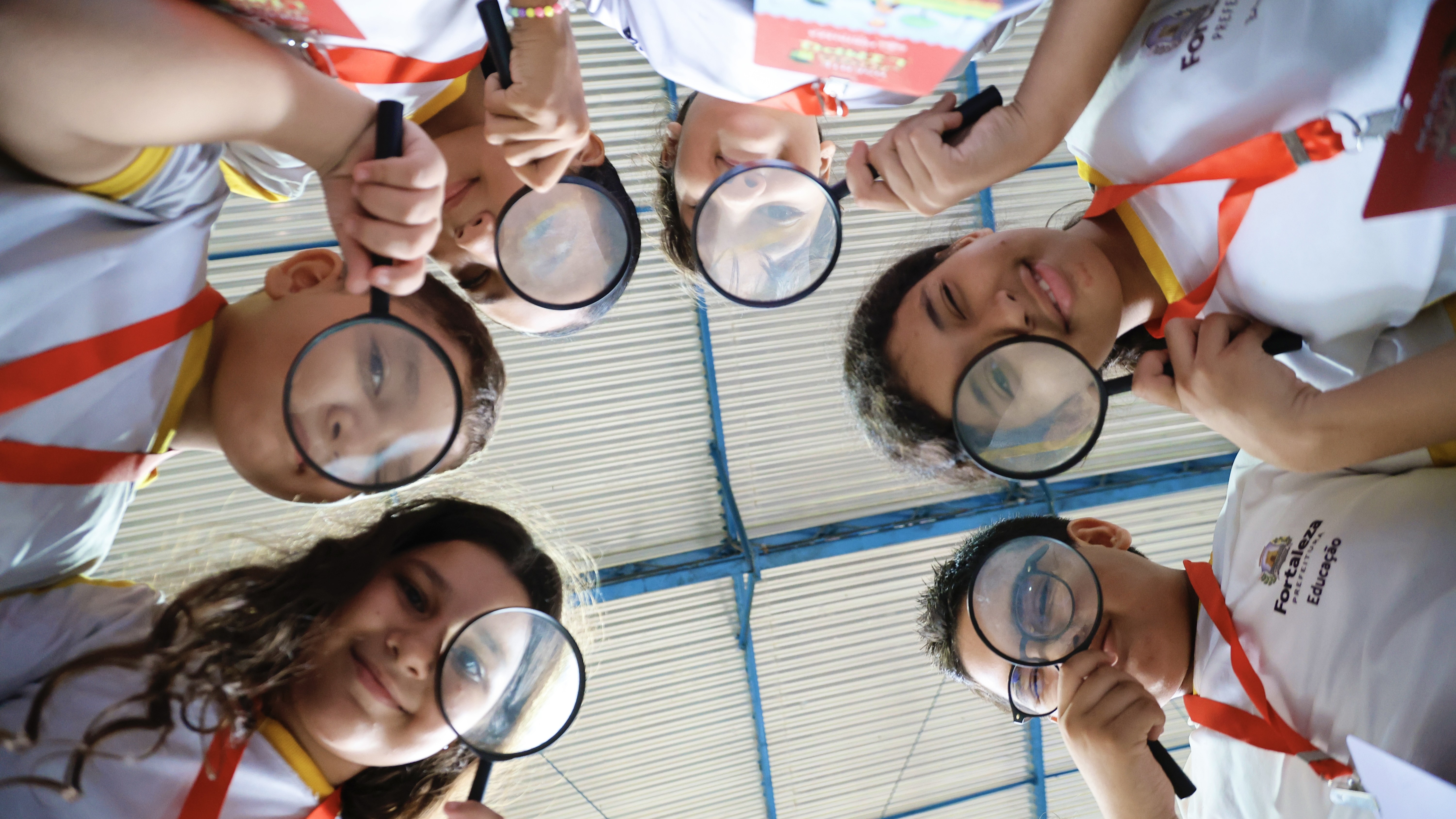 a foto mostra estudante em uma roda e todos usam uma lupa